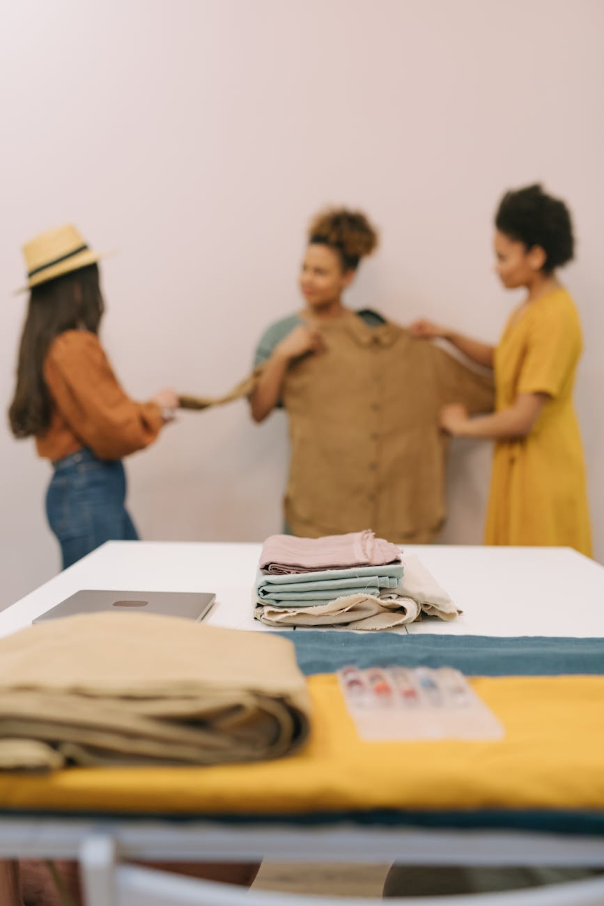 women looking at a brown blouse behind a table with a pile of folded fabric